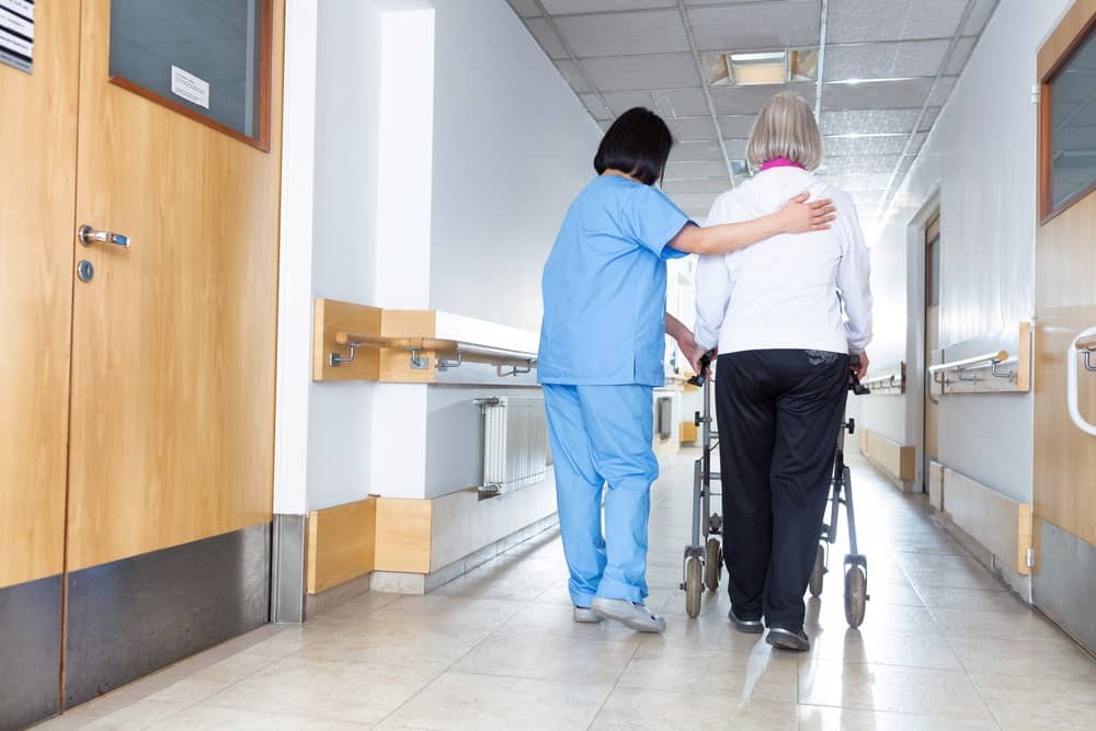 Pflegefachkraft finden - Pflegerin mit Patientin im Krankenhausgang